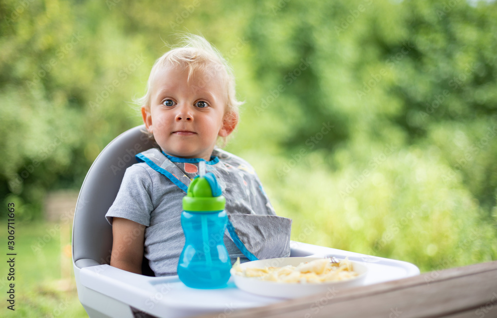 Cute baby sitting in high chair at the dinning table outdoor