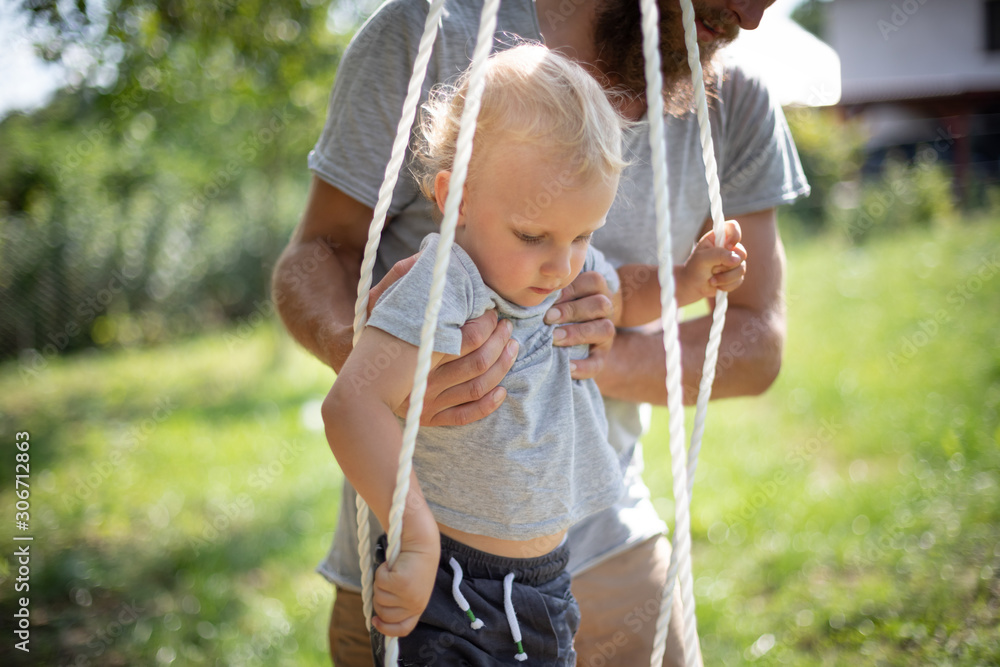 Dad puts this small child in a swing on backyard