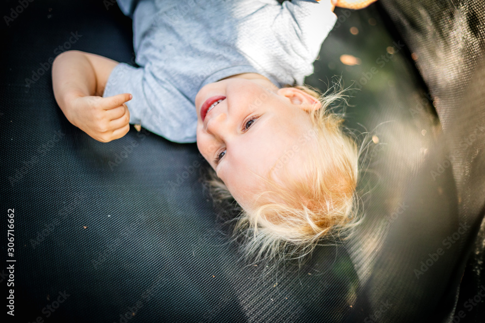 Little child playing and jumping on trampoline outdoor in backyard