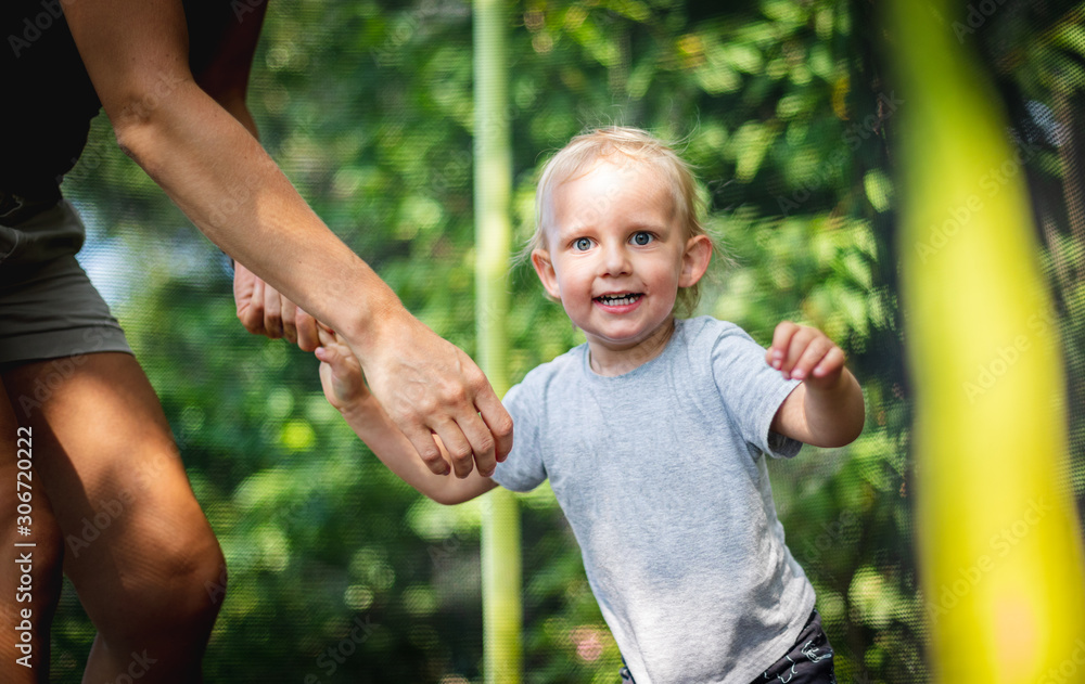 Little child with his mom playing on trampoline outdoor in backyard