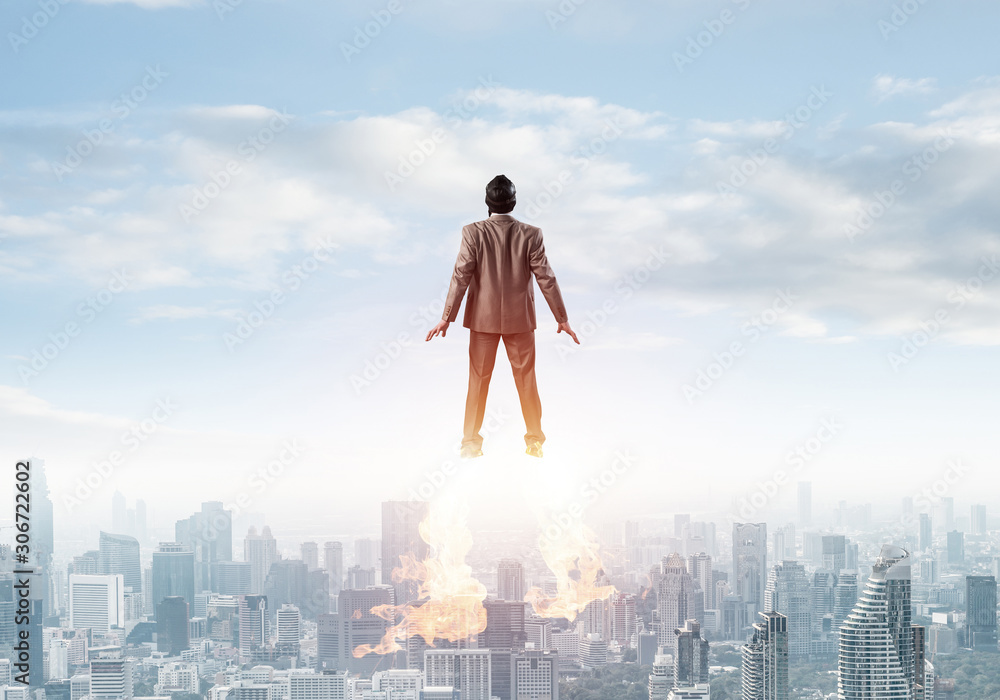 Businessman in suit and aviator hat flying in sky