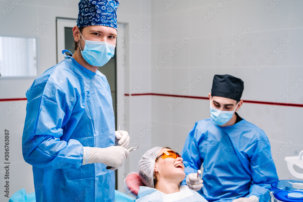 Doctor wearing blue coat and mask inviting you to dentist office and looking at camera with stomatol