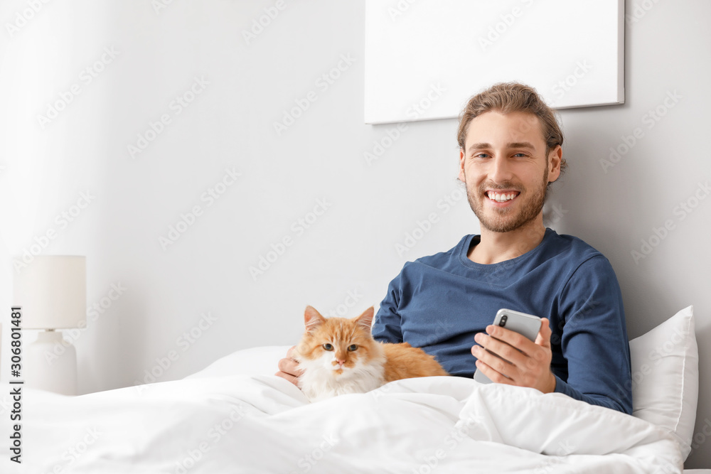 Man with mobile phone and his cute cat in bedroom