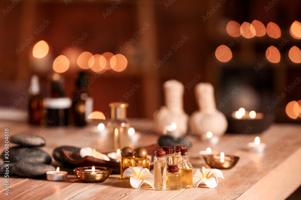 Bottles of essential oil, flowers and candles on table in spa salon