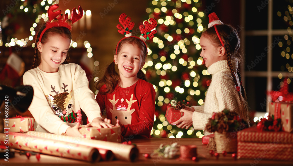 happy funny children girls pack Christmas gifts at evening in home.