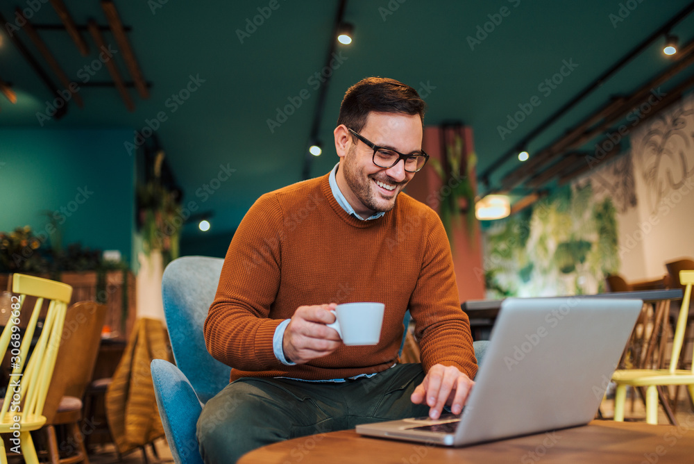 Freelancer working on laptop in a cafe, smiling and drinking coffee, portrait.