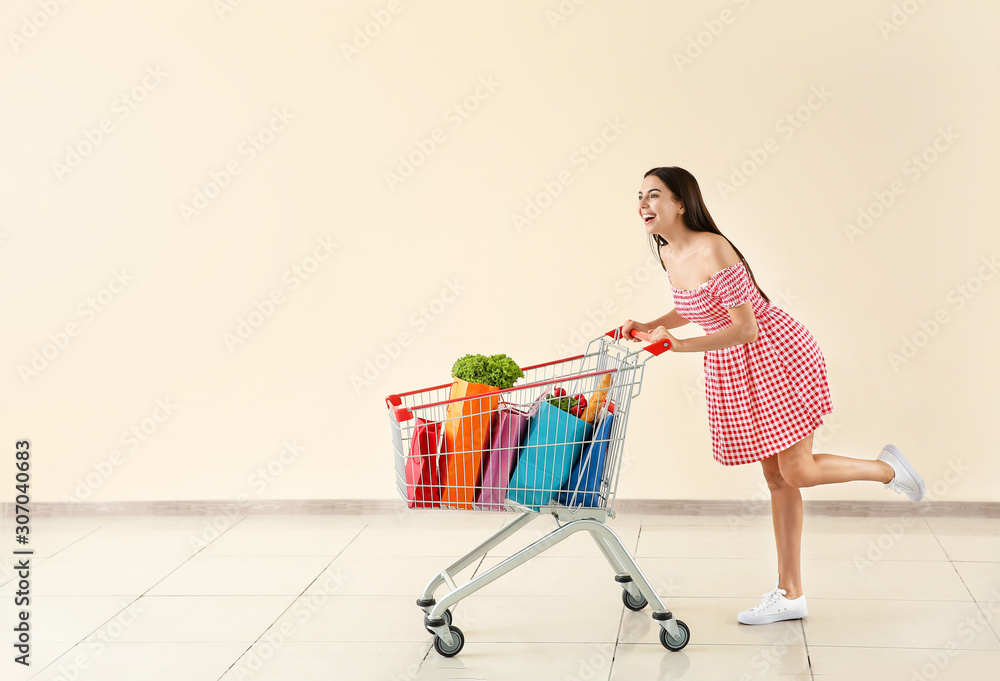 Young woman with shopping cart near light wall