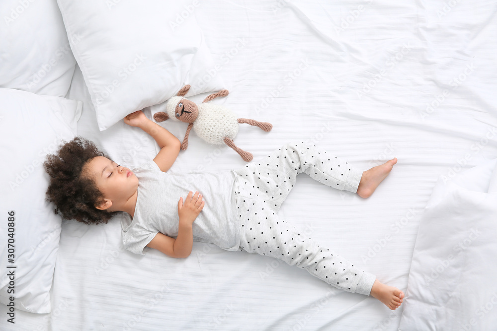 Little African-American girl with toy sleeping in bed