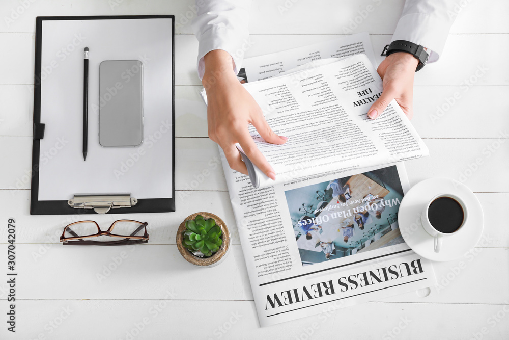 Young businesswoman reading newspaper at table