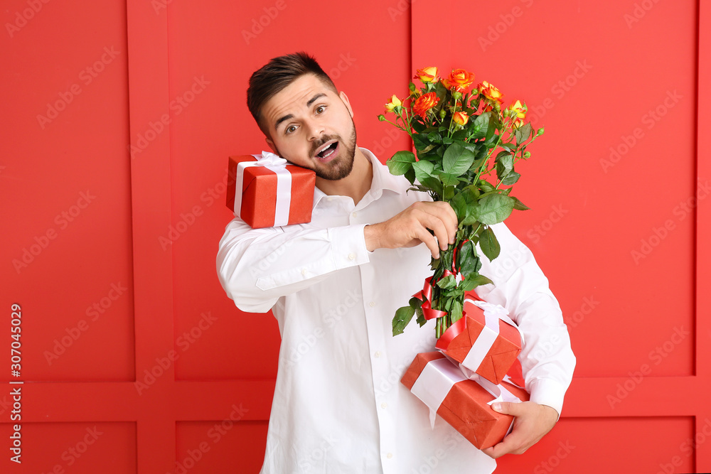 Handsome man with flowers and gifts on color background. Valentines Day celebration