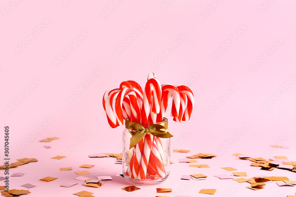 Glass jar with Christmas candy canes on color background