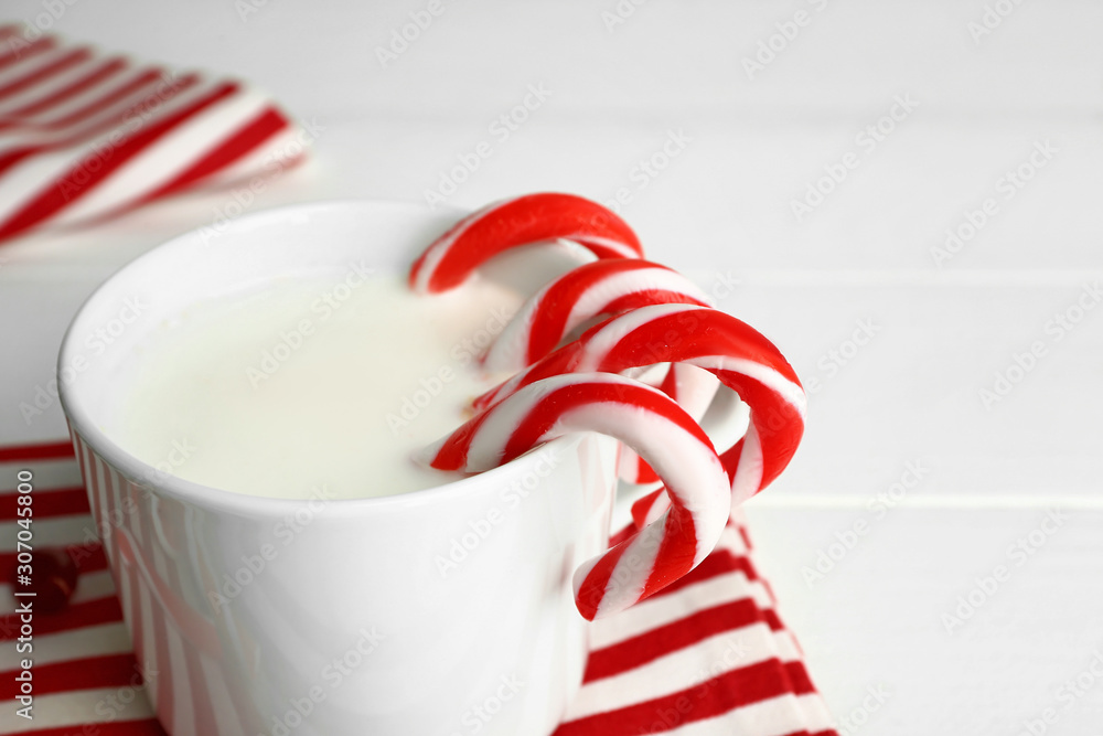 Cup of milk with Christmas candy canes on table