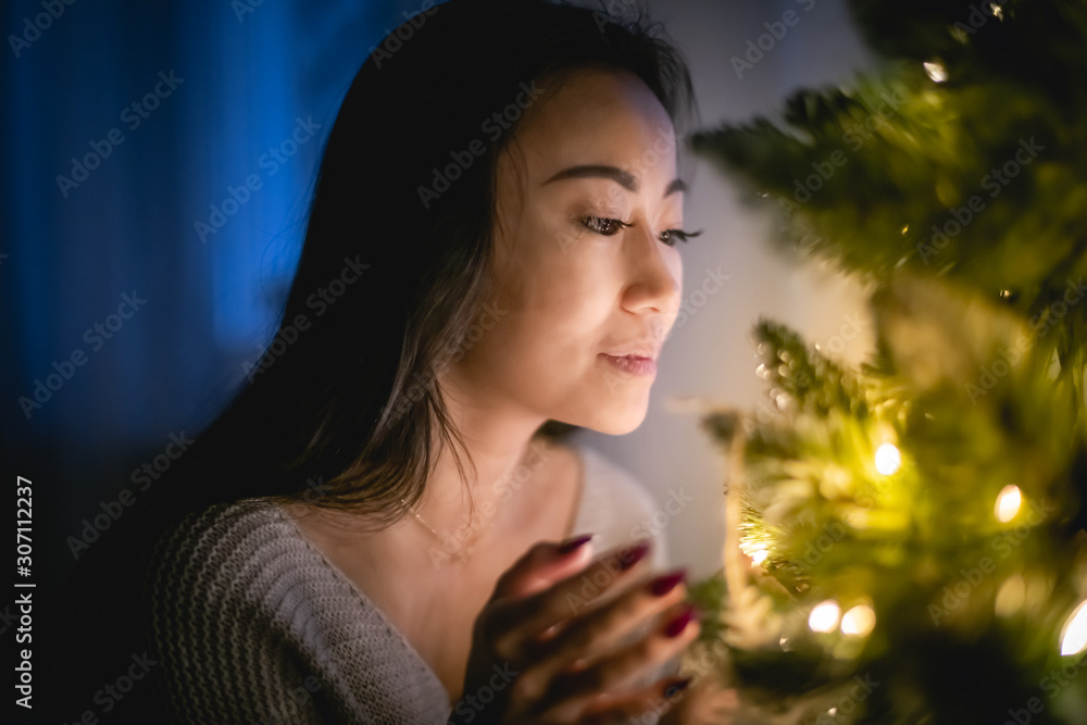 美丽的亚洲女人晚上在家里装饰圣诞树