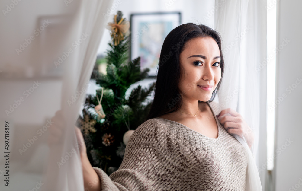 Happy asian woman standing near window in christmas decorated home