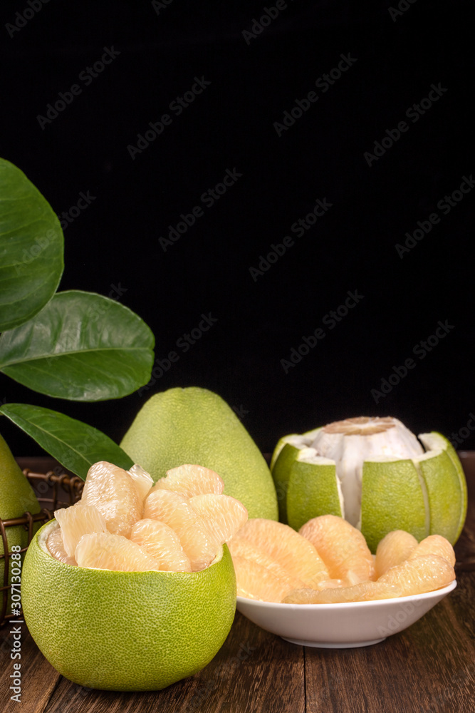 Fresh peeled pomelo, grapefruit, shaddock with green leaves on dark wooden plank table. Seasonal fru