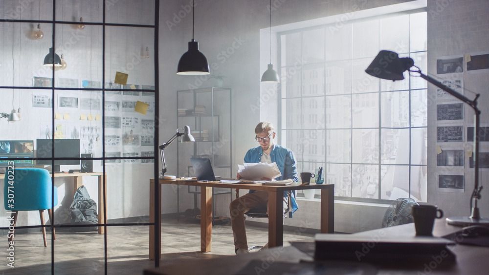 Shot of a Young Creative Designer Works on Laptop at His Desk, He Browses Through Concept Sketches. 