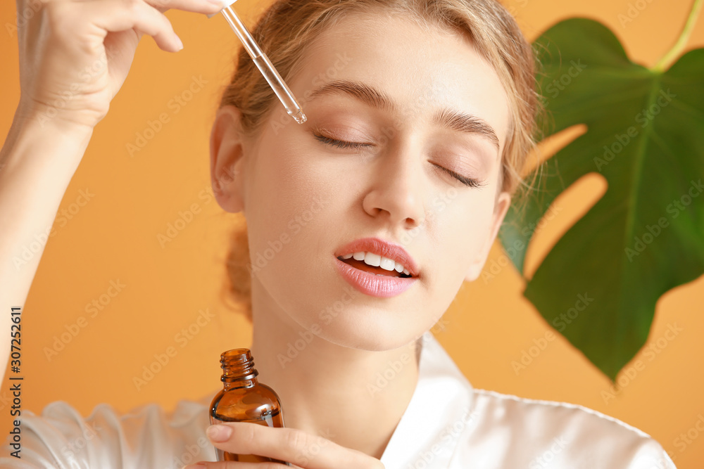 Beautiful young woman with cosmetic product on color background