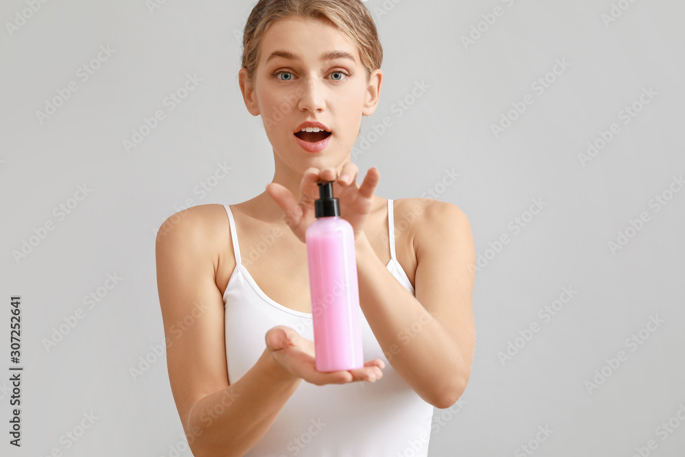 Beautiful young woman with cosmetic product on light background