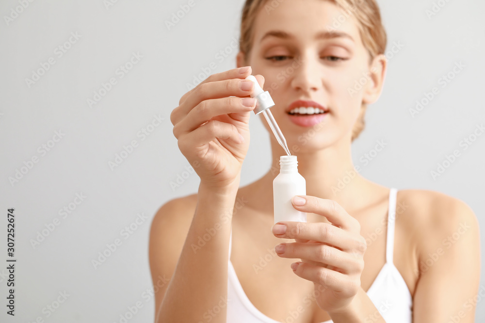 Beautiful young woman with cosmetic product on light background