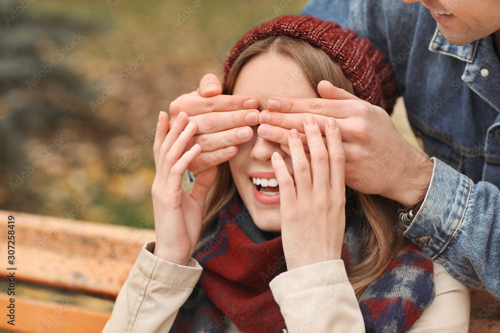 Man covering eyes of his girlfriend sitting on bench in park