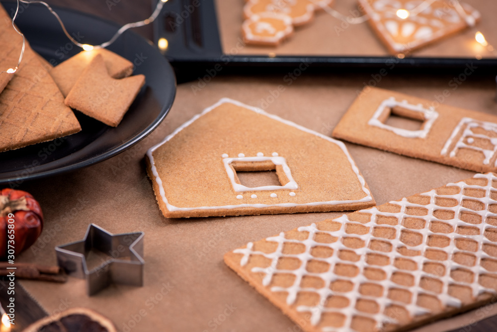 Woman is decorating gingerbread cookies house with white frosting icing cream topping on wooden tabl