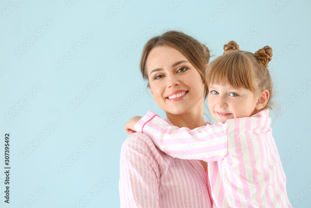 Portrait of happy mother and daughter in pajamas on color background