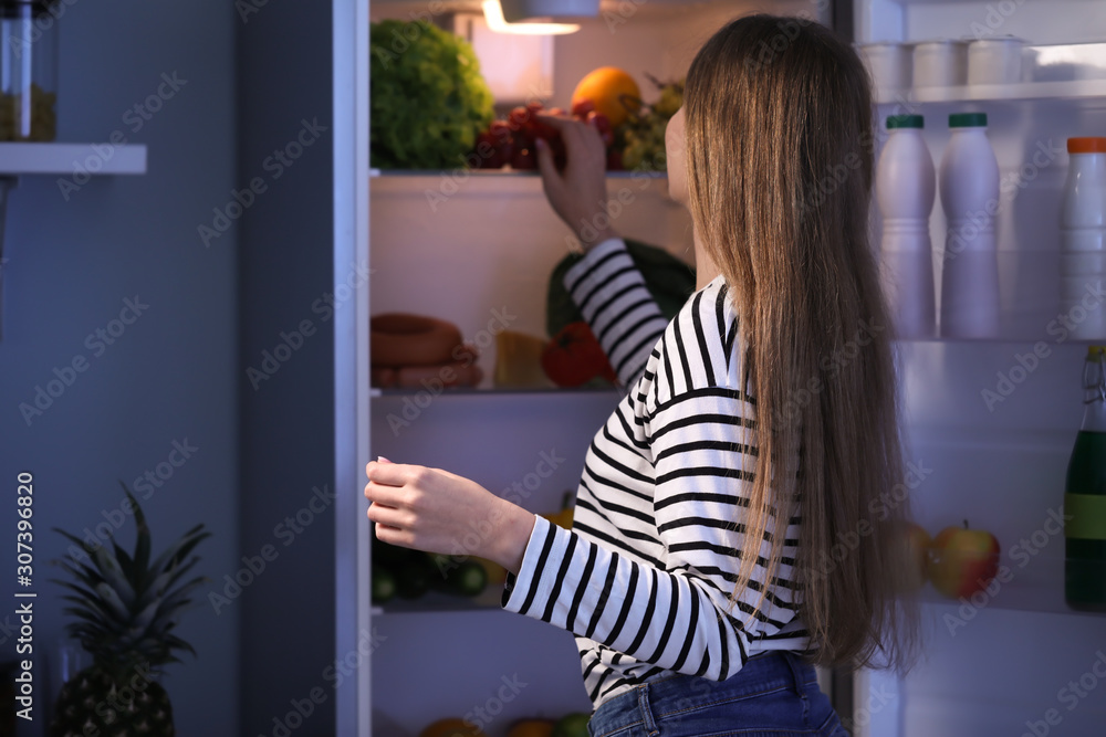 美丽的年轻女子晚上在冰箱里挑选食物