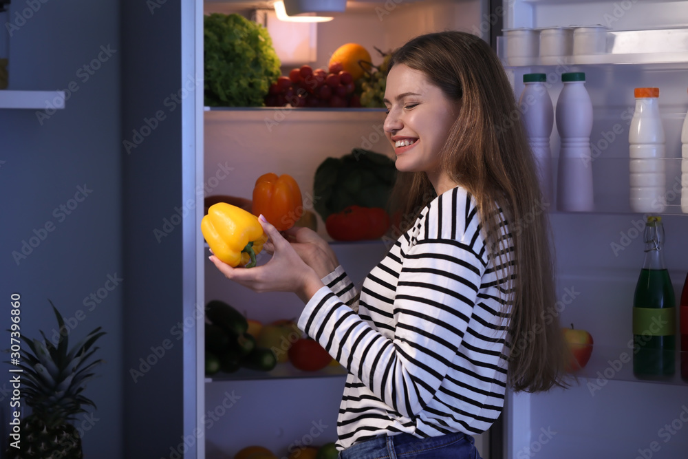 美丽的年轻女子晚上在冰箱里挑选食物