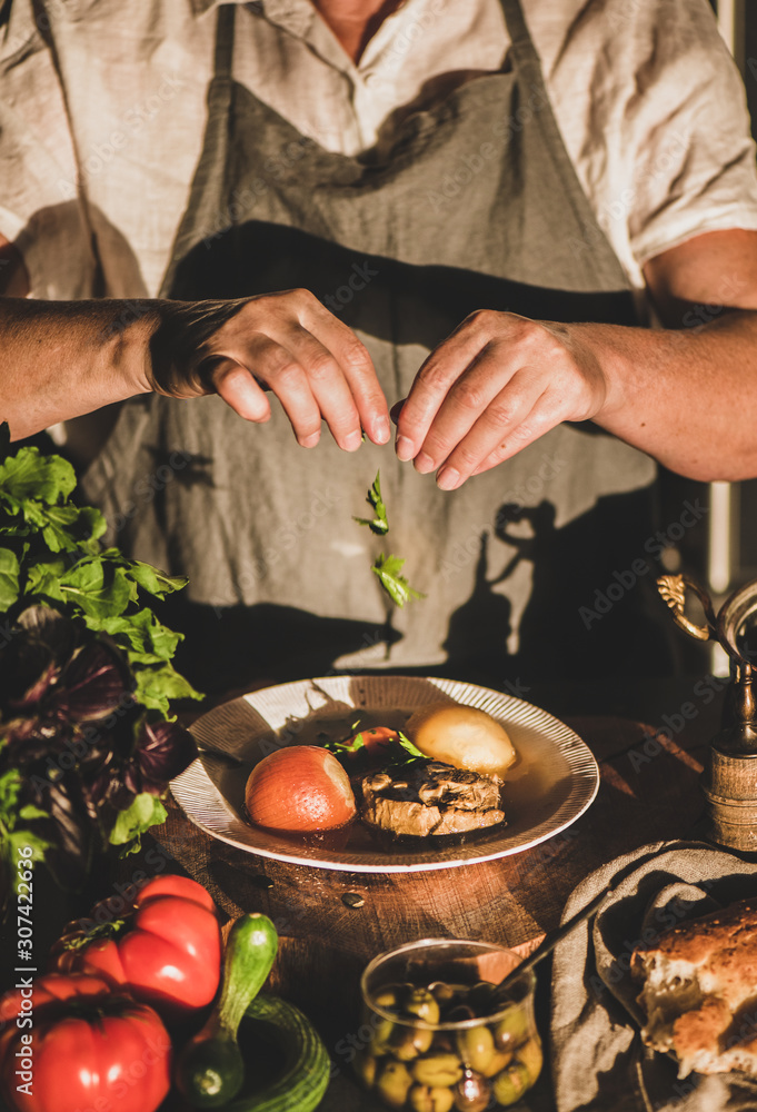 Eldery woman in linen apron putting herbs toTurkish traditional meat soup Haslama with vegetables in