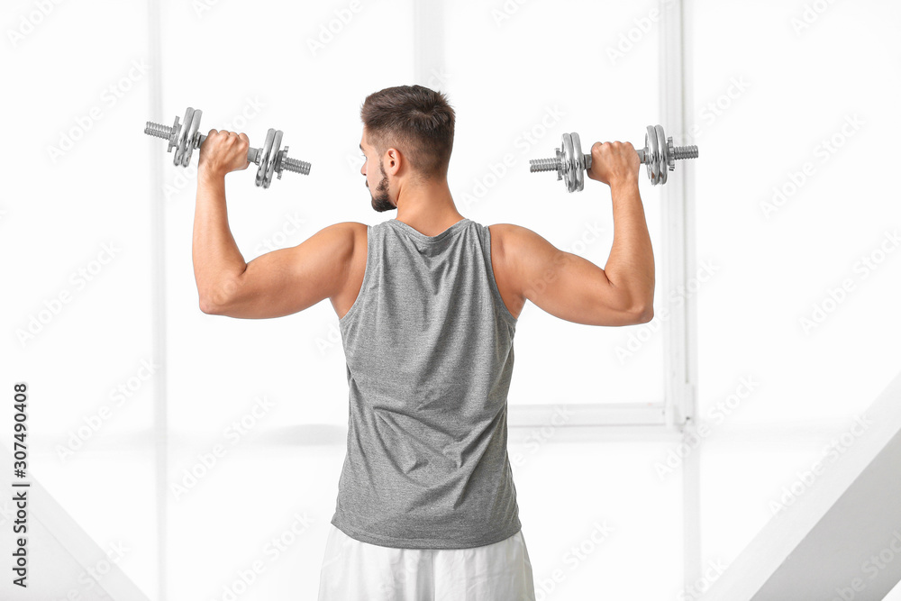 Sporty young man training with dumbbells in gym