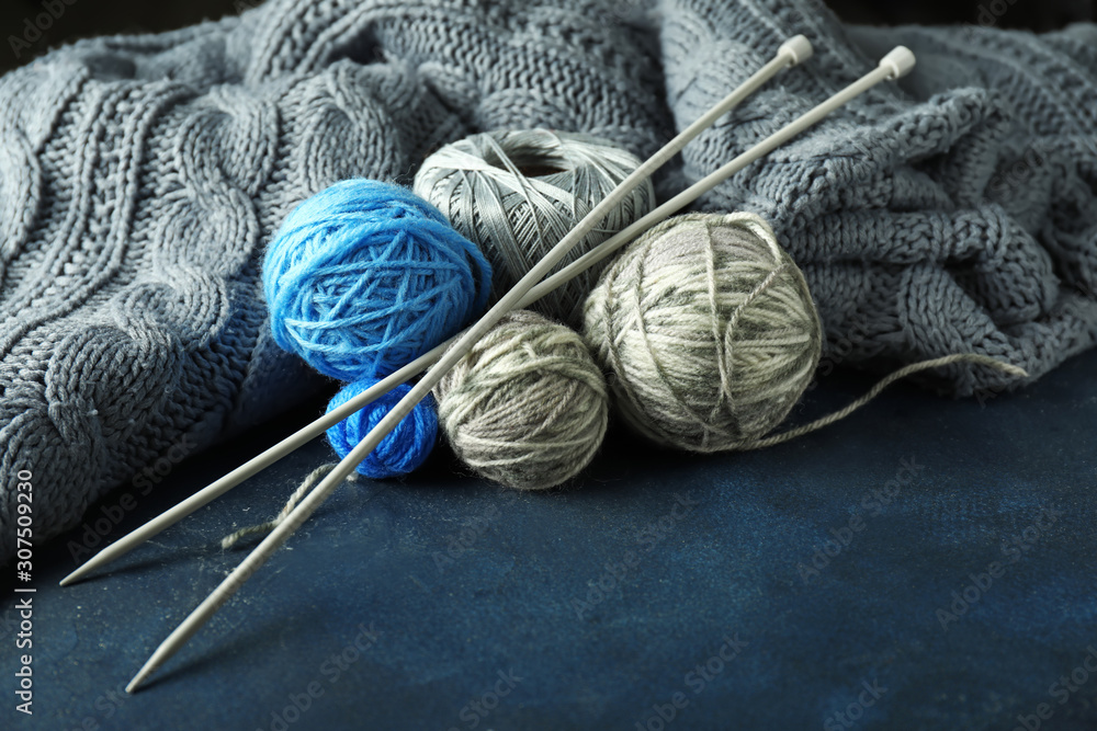 Knitted clothes, yarns and needles on color background