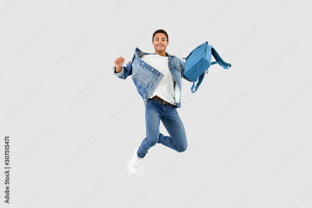 Jumping African-American teenager boy with backpack on white background