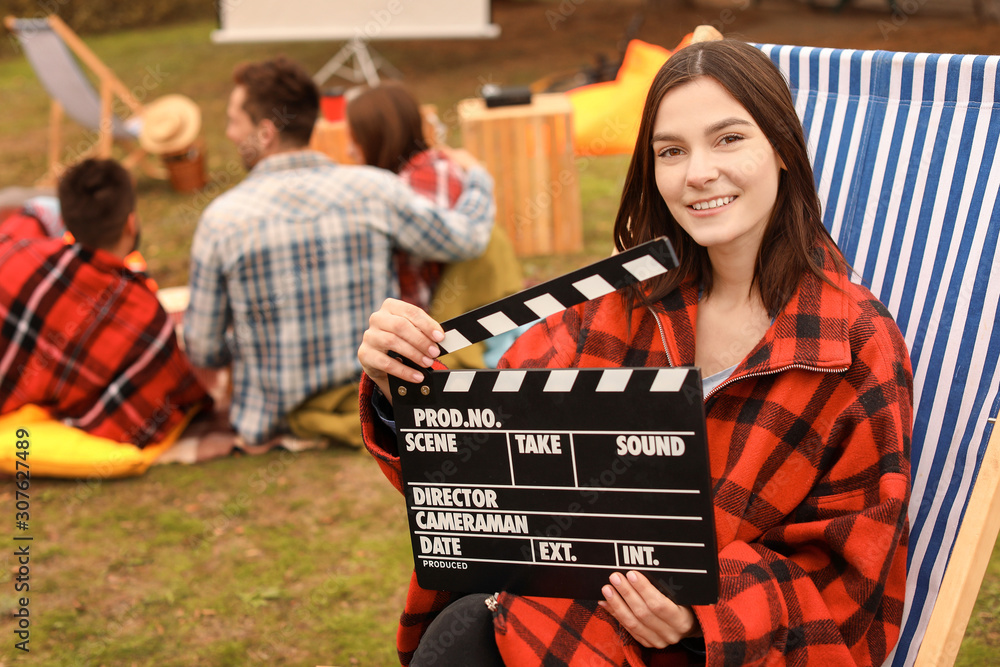 Happy young woman with movie clapper in outdoor cinema