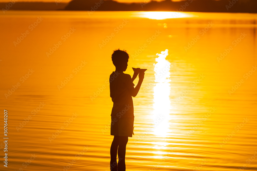 Paper boat is in the hands of a child. Beautiful summer sunset. Origami. Silhuette against sundown. 