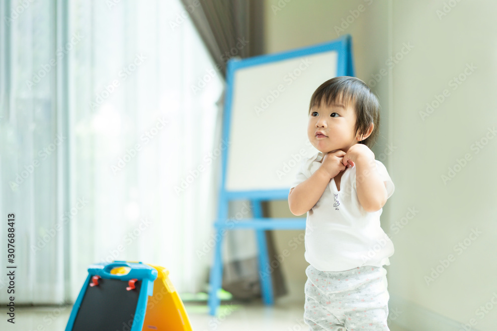 Asian cute baby standing and playing  toy at home. The kid looking aside and make a question face ab