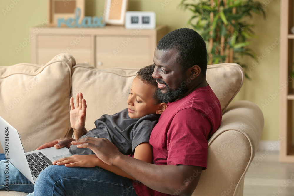 Portrait of African-American man and his little son with laptop at home