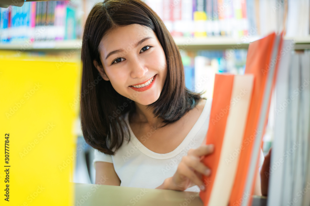 快乐的亚洲女学生女孩在课间休息时在书架附近看书