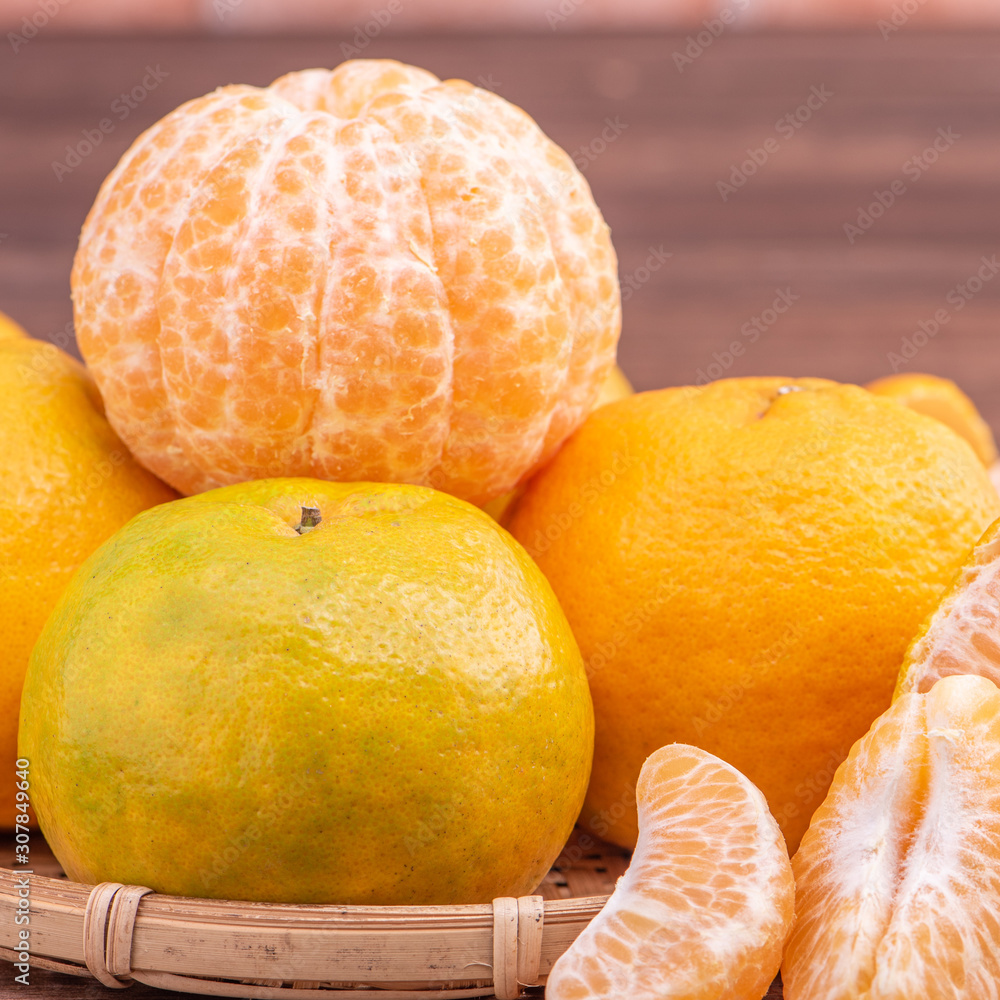 Peeled tangerines in a bamboo sieve basket on dark wooden table with red brick wall background, Chin