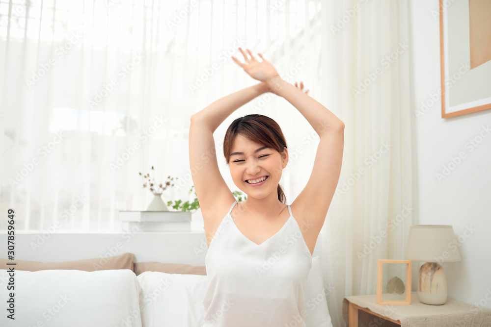 Happy Asian girl waking up stretching arms sitting on the bed in the morning