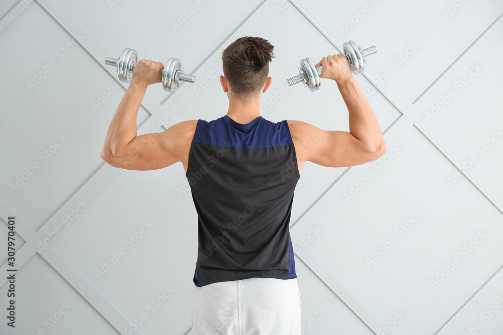 Sporty young man with dumbbells on light background