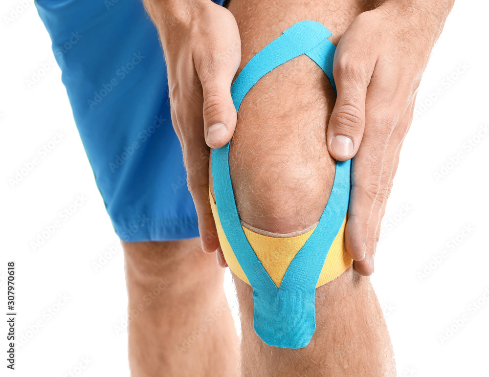 Sporty man with physio tape applied on knee against white background, closeup