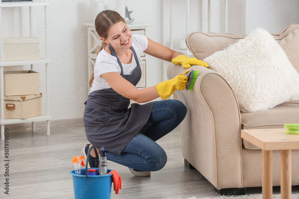 Female janitor cleaning furniture in room