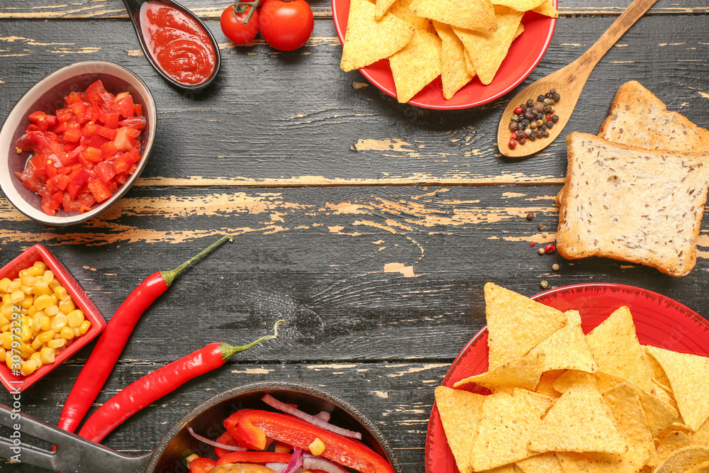 Frame made of tasty nachos and products on dark wooden background