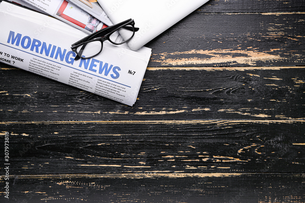 Newspapers and laptop on dark wooden background