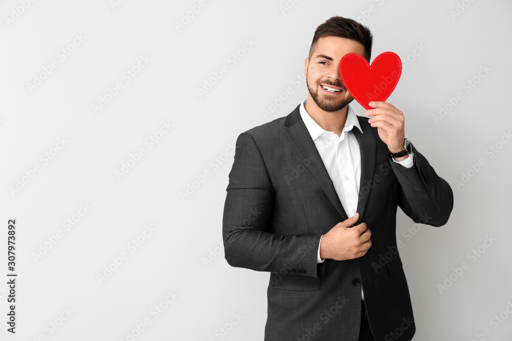 Handsome man with red heart on light background. Valentines Day celebration