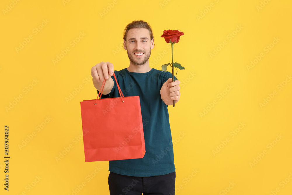 Handsome man with flower and gift on color background. Valentines Day celebration