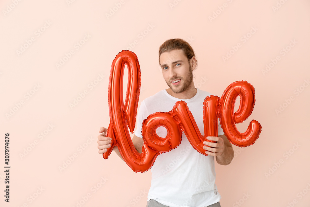 Handsome man with air balloon in shape of word LOVE on color background. Valentines Day celebration