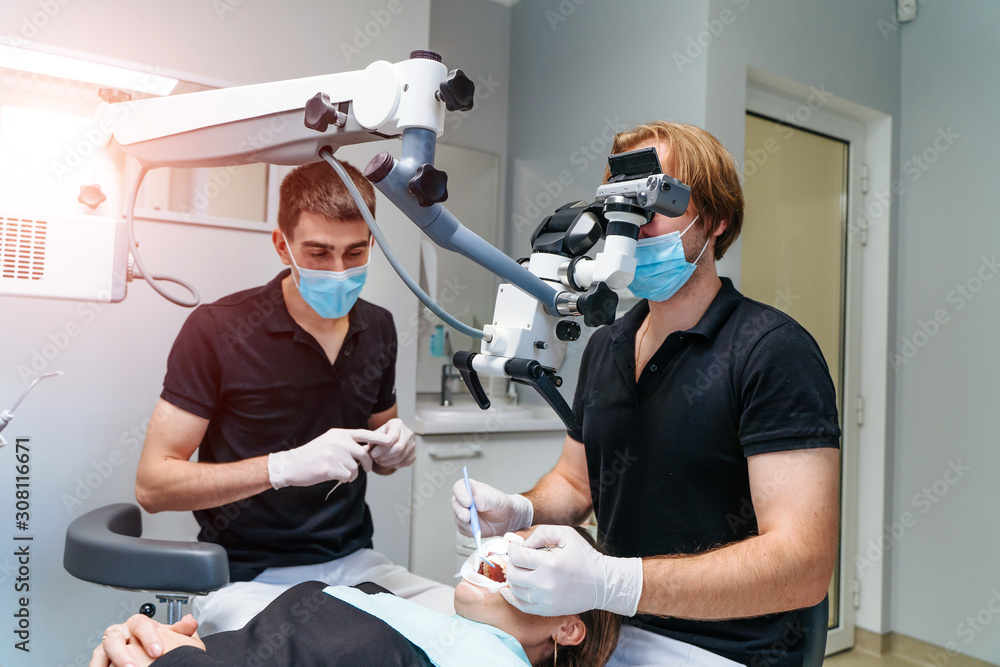 Male dentist with dental tools - microscope, mirror and probe treating patient teeth at dental clini