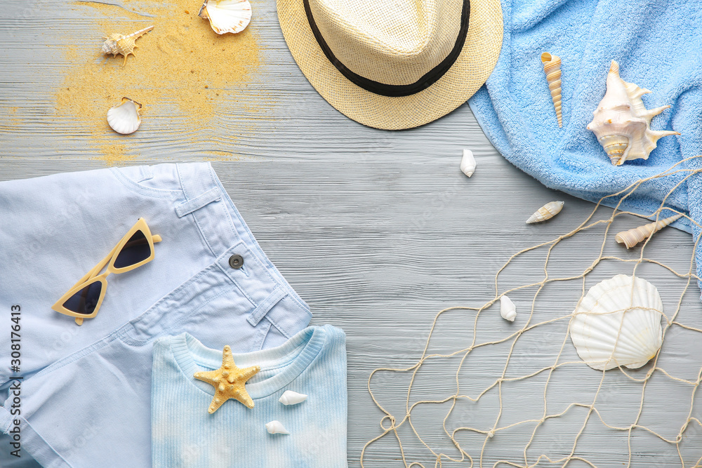 Set of beach accessories with clothes and seashells on wooden background