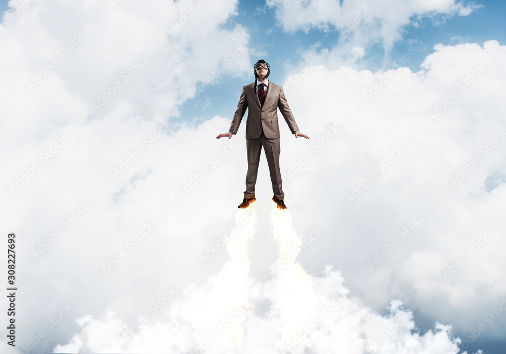 Businessman in suit and aviator hat flying in sky